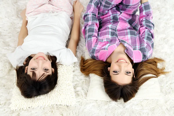 Δύο κορίτσια στο πιτζάμες ξαπλωμένο στο χνουδωτό λευκό χαλί, στο ανοιχτό φόντο — Φωτογραφία Αρχείου