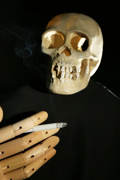 Totenkopf und Holzhand mit Zigarette auf dunklem Hintergrund — Stockfoto