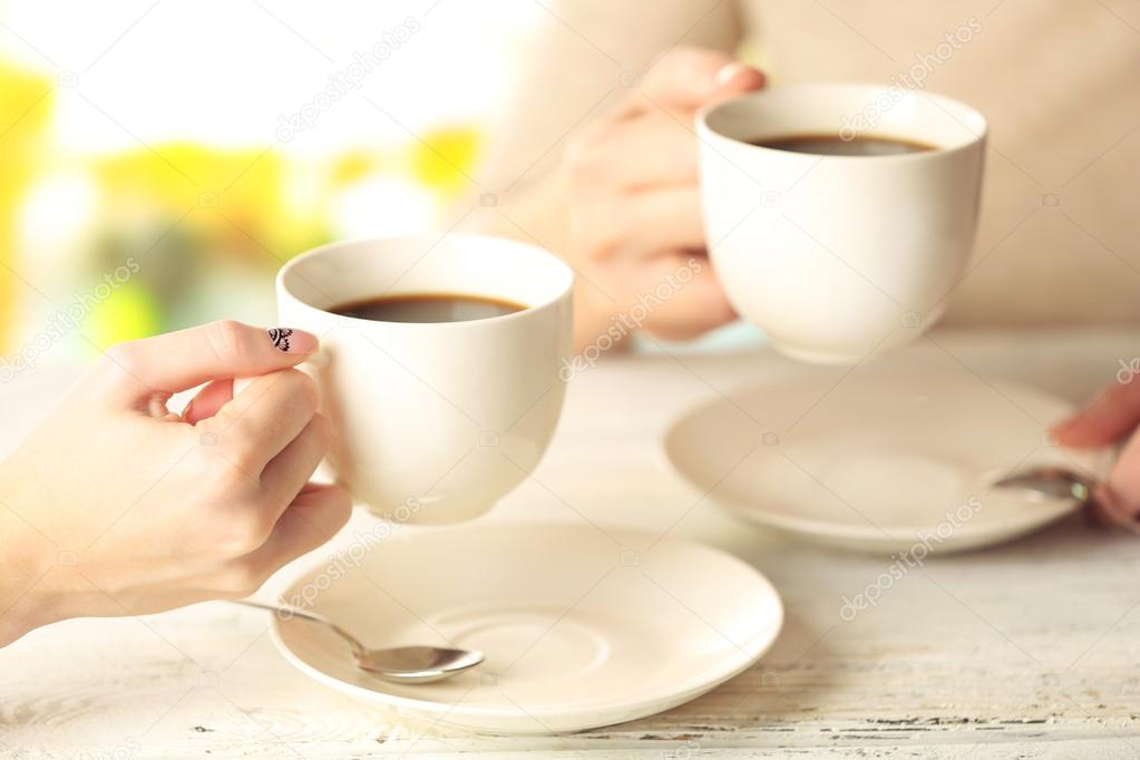 Two women with cups of coffee on bright background