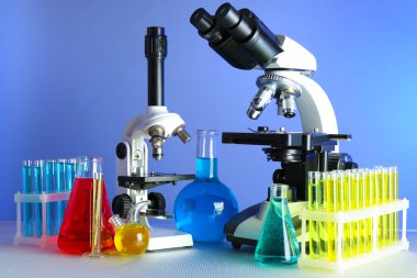 Mikroskoplar ve test tüpleri masada, renk arkaplanında