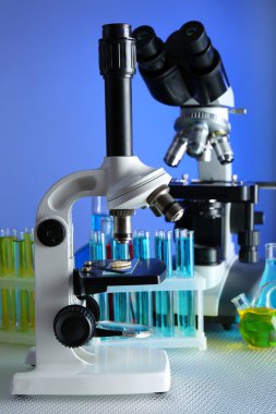 Mikroskoplar ve test tüpleri masada, renk arkaplanında