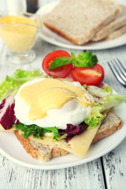Yumurta Benedict ile tost ve ahşap masa üzerinde tabakta domates