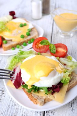 Yumurta Benedict ile tost ve ahşap masa üzerinde tabakta domates
