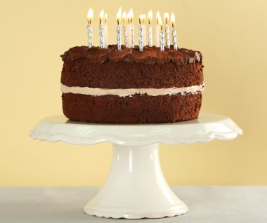 Bej renkli arka plan üzerinde masada mumlarla lezzetli çikolatalı kek