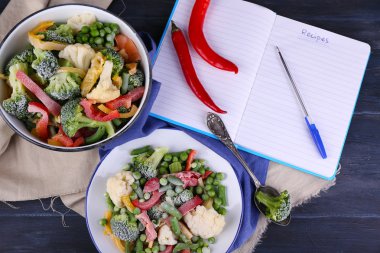 Dondurulmuş sebzeler ve ahşap masa arka plan üstünde boş defter