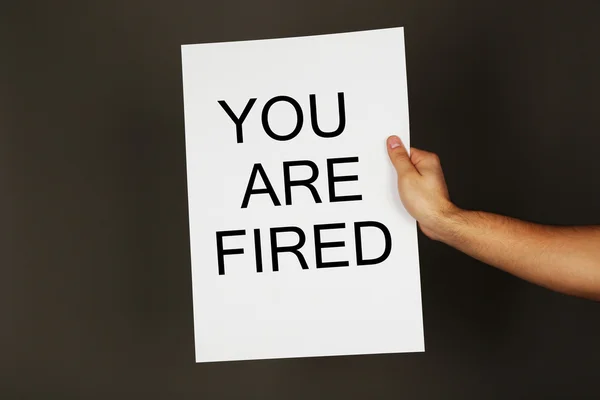 Sheet of paper with text You Are Fired in male hand on dark background — Stock Photo, Image