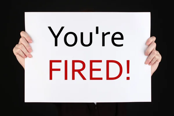 Sheet of paper with text You're Fired in hands isolated on black — Stock Photo, Image