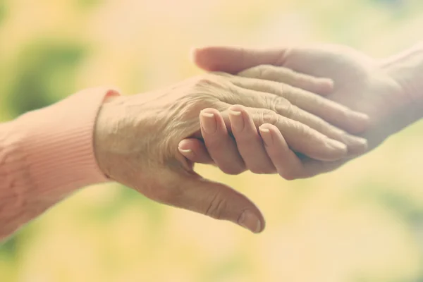 Old and young holding hands on light background, closeup — Stok Foto