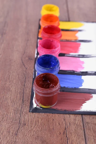 色彩斑斓的油漆笔迹，白色纸片上的油漆罐，木制桌子背景 — 图库照片