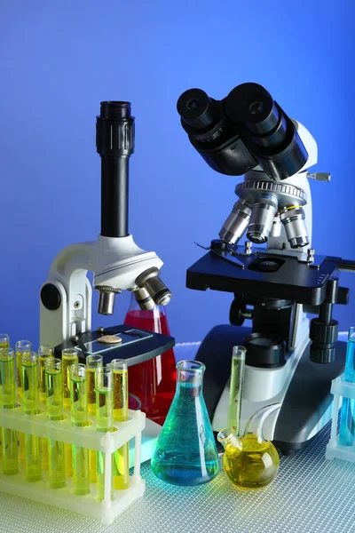 Mikroskoplar ve test tüpleri masada, renk arkaplanında
