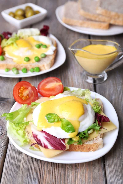 Toast with egg Benedict and tomato on plate on wooden table — Stock Photo, Image