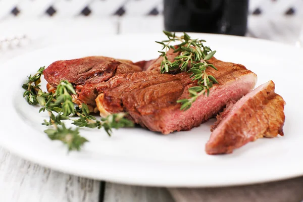 Steak with herbs on plate on wooden table — Stock Photo, Image