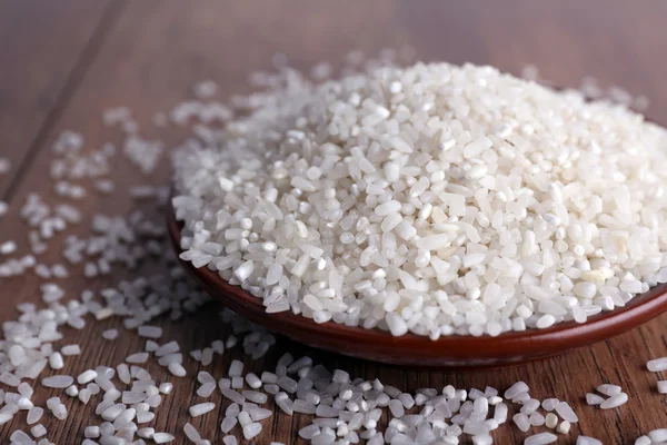 Grain of rice on plate on wooden background — Stock Photo, Image