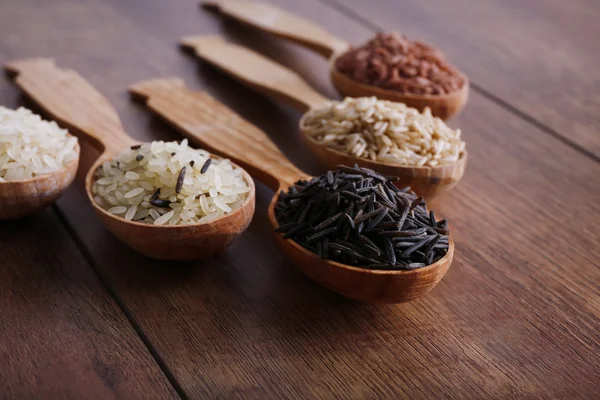 Diferentes tipos de arroz en cucharas sobre fondo de madera — Foto de Stock