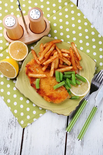 Breaded fried fish fillets and potatoes with asparagus and sliced lemon on plate and wooden planks background — Stock Photo, Image