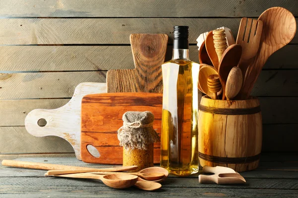 Деревянные кухонные принадлежности со стеклянной бутылкой оливкового масла на фоне деревянных досок — стоковое фото