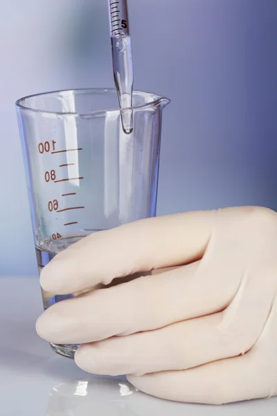 Main de l'assistant avec liquide dans la verrerie pendant l'expérience en laboratoire sur fond flou clair — Photo