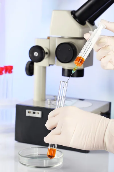 Asistente de manos en guantes haciendo análisis en laboratorio con microscopio y fondo borroso — Foto de Stock