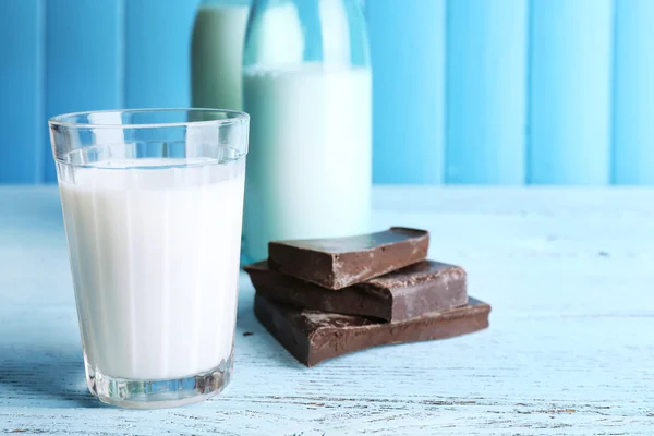 Glas och flaskor av mjölk med choklad bitar på färg träplankor bakgrund — Stockfoto