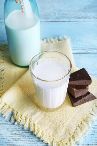 Glass and bottle of milk with chocolate chunks on color wooden planks background — Stock Photo, Image