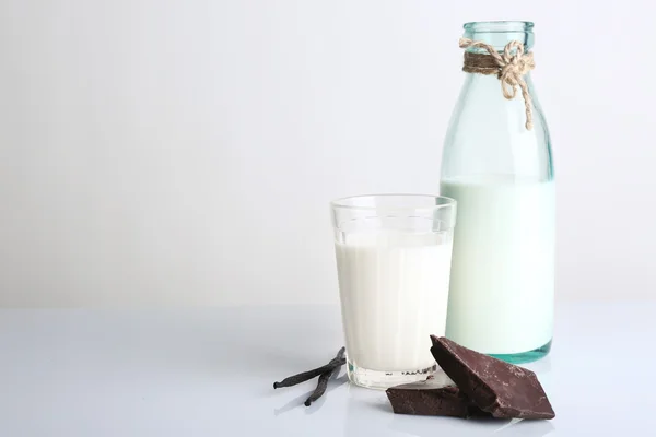 Bicchiere e bottiglia di latte con pezzi di cioccolato e bastoncini di vaniglia isolati su bianco — Foto Stock