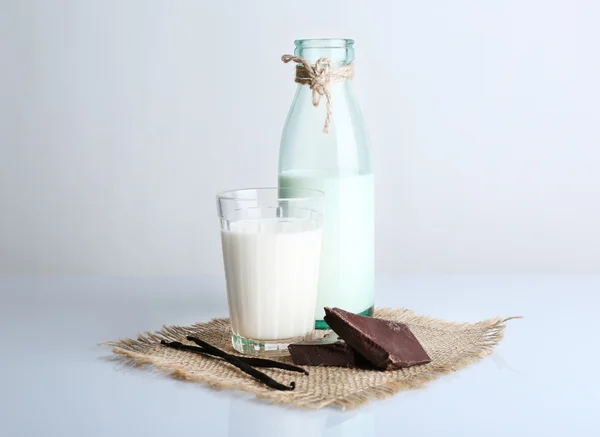 Bicchiere e bottiglia di latte con pezzi di cioccolato e bastoncini di vaniglia su tela isolata su bianco — Foto Stock