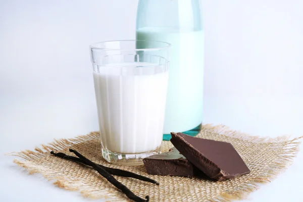 Glass and bottle of milk with chocolate chunks and vanilla sticks on burlap cloth isolated on white — Stock Photo, Image