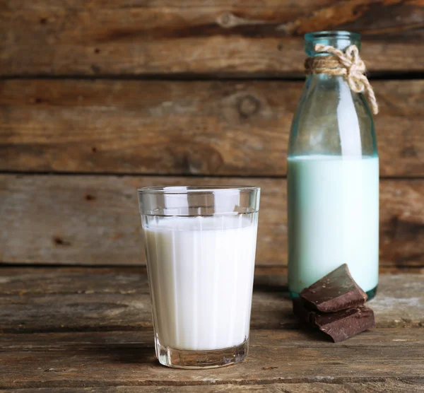Bicchiere e bottiglia di latte con pezzi di cioccolato su tavole di legno rustico sfondo — Foto Stock