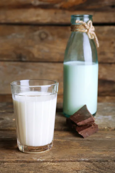 Glass and bottle of milk with chocolate chunks on rustic wooden planks background — Stock Photo, Image