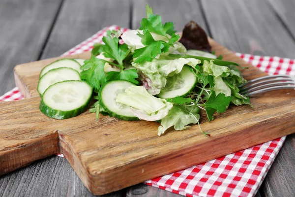 Sliced cucumber and greens on cutting board and wooden planks background — Stock Photo, Image