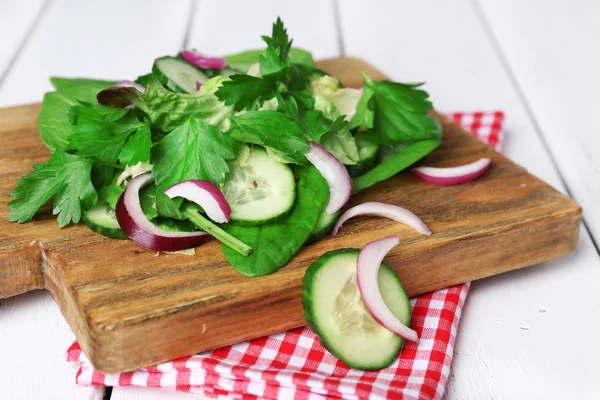Mezcle las hojas de ensalada con pepino en rodajas y cebolla en la tabla de cortar y el fondo de tablones de madera de color —  Fotos de Stock
