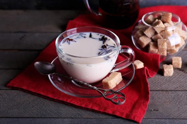 红茶牛奶和方糖在玻璃器皿上彩色木板背景 — 图库照片