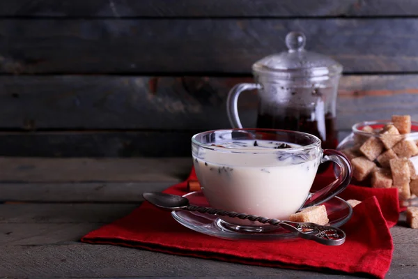 Tè nero con latte e zucchero grumo in vetreria su sfondo tavole di legno colore — Foto Stock