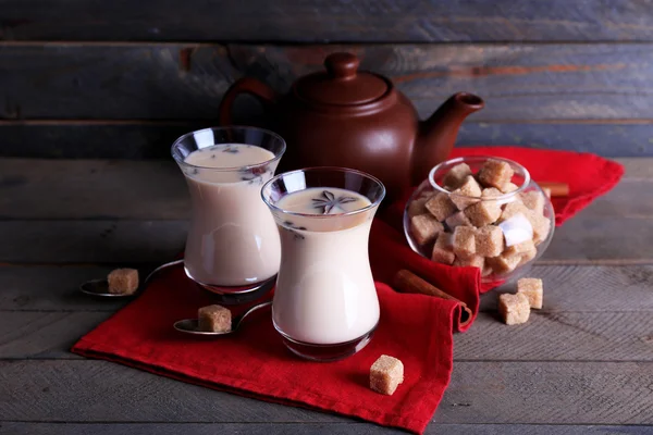 Schwarzer Tee mit Milch in Gläsern und Teekanne mit Klumpen Zucker auf farbigen Holzplanken Hintergrund — Stockfoto