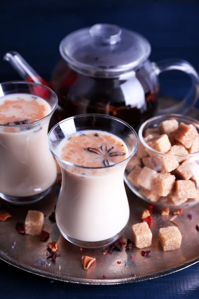 Black tea with milk in glasses and teapot with lump sugar on metal tray and color wooden planks background — Stock Photo, Image