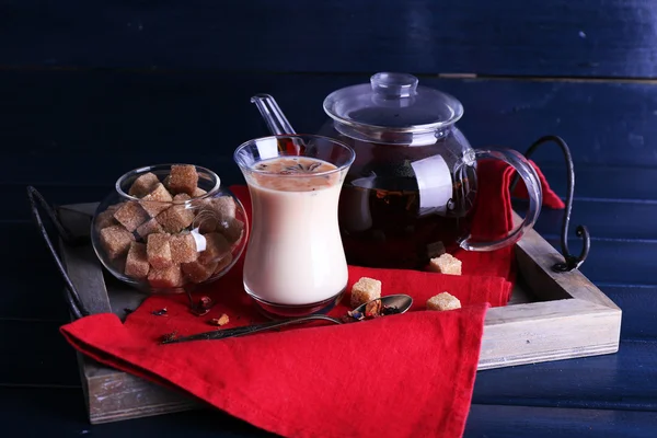 Black tea with milk and lump sugar on wooden tray with napkin and color wooden planks background — Stock Photo, Image