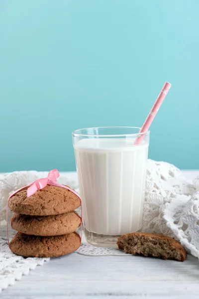 Sabrosas galletas y vaso de leche en la mesa de madera de color, sobre fondo brillante — Foto de Stock