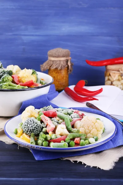 Bevroren groenten op plaat op servet, op houten tafel achtergrond — Stockfoto