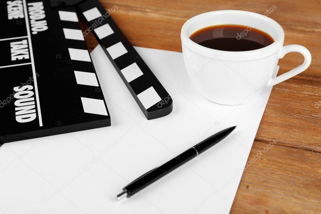 Movie clapper with paper, pen and cup of coffee on wooden planks background