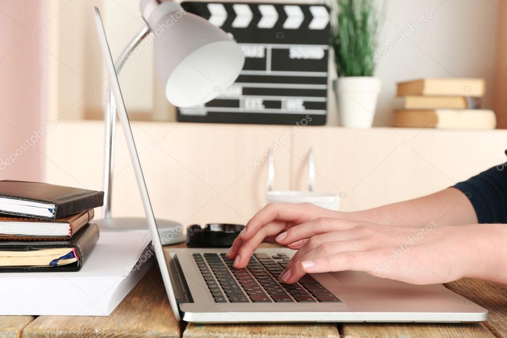 Female hands of scriptwriter working on laptop at desk on cupboard background
