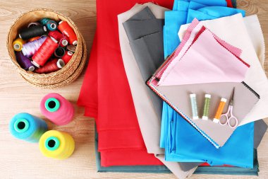 Ahşap masa arkasında renkli kumaş örnekleri, iplikler ve makas