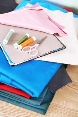 Ahşap masa arkasında renkli kumaş örnekleri, iplikler ve makas