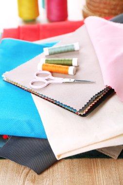 Ahşap masa arkasında renkli kumaş örnekleri, iplikler ve makas