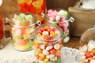 Ahşap arka plan üzerinde cam kavanozlara çok renkli şekerler