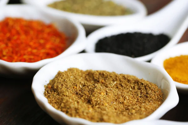 Different kinds of spices in ceramics spoons, close-up, on wooden background — Stock Photo, Image