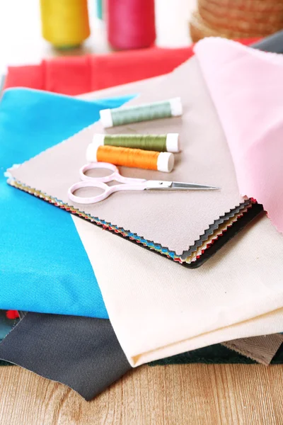 Colorful fabric samples, threads and scissors on wooden table background — Stock Photo, Image