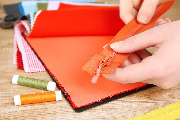 Colorful fabric samples and zipper in female hands on wooden table background — Stock Photo, Image