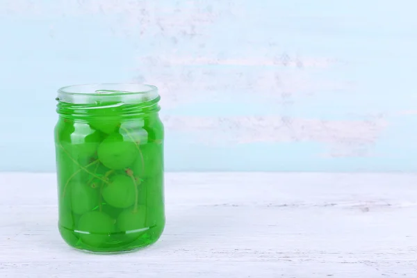 Homemade jar of green maraschino cherry on wooden table and color wall background