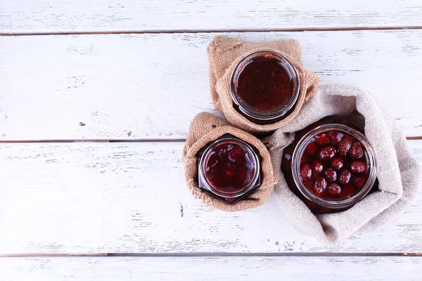 Homemade jars of fruits jam in burlap pouches on color wooden planks background — Stock Photo, Image