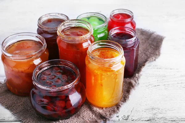 Homemade jars of fruits jam on color wooden planks background — Stock Photo, Image